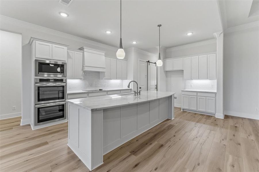 Modern kitchen featuring a large central island with seating, pendant lighting, built-in stainless steel appliances, and wood-finish flooring Modern kitchen featuring a large central island with seating, pendant lighting, built-in stainless steel appliances, and wood-finish flooring