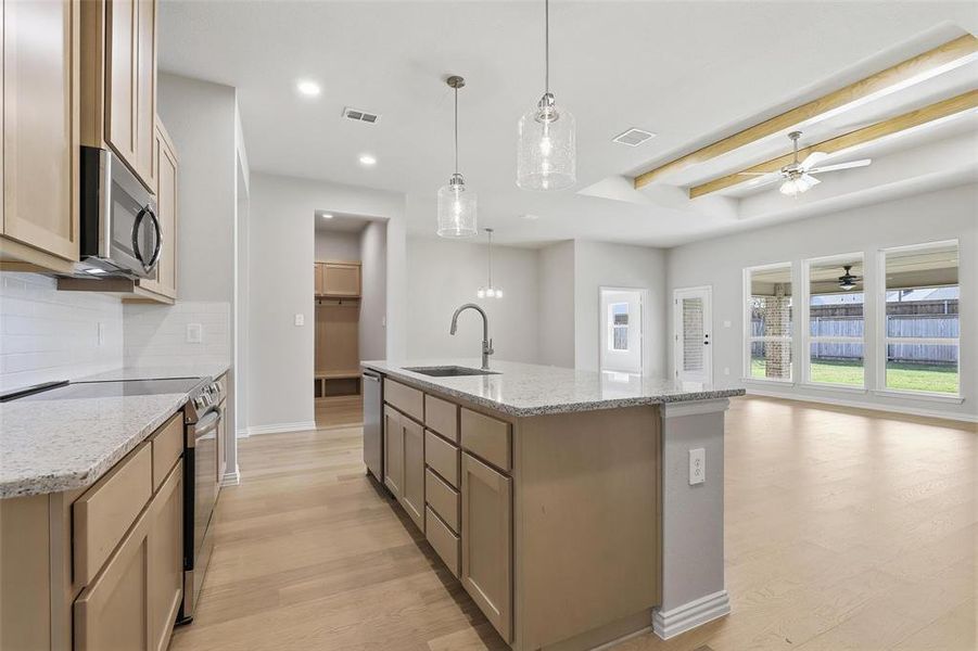 Kitchen featuring appliances with stainless steel finishes, light stone countertops, light wood-style flooring, hanging light fixtures, and tasteful backsplash Kitchen featuring appliances with stainless steel finishes, light stone countertops, light wood-style flooring, hanging light fixtures, and tasteful backsplash