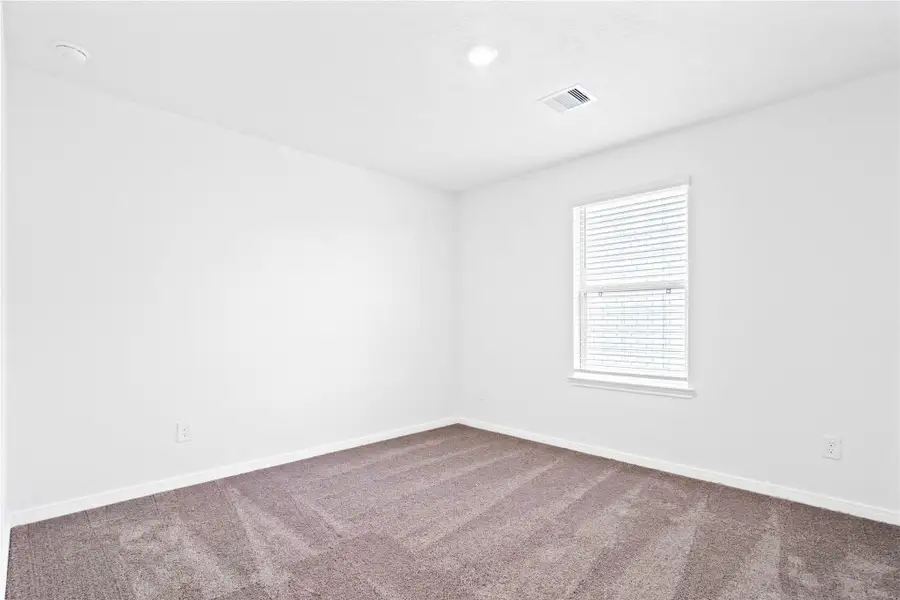This secondary bedroom offers comfort and style with plush carpeting, neutral paint tones, recessed lighting, a large window with blinds, and a walk-in closet.