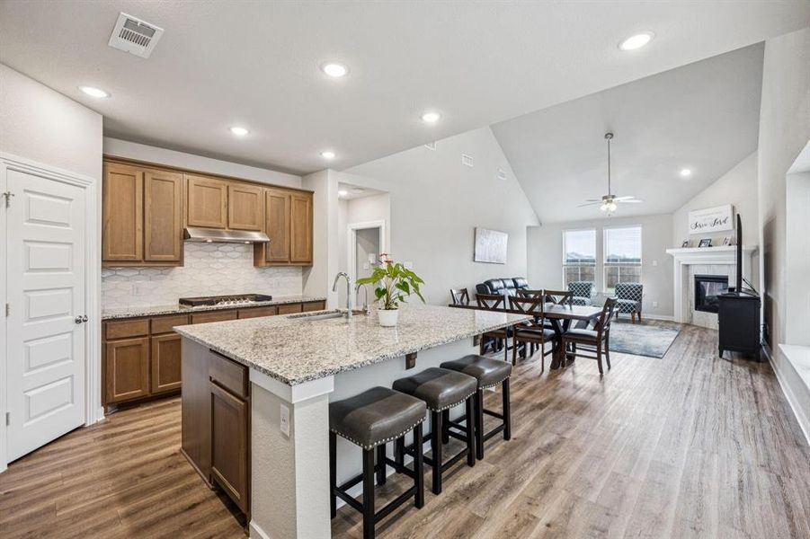 Kitchen with backsplash, light stone counters, a kitchen bar, an island with sink, and vaulted ceiling