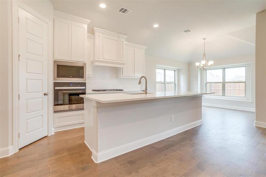 Kitchen with light wood-type flooring, a center island with sink, backsplash, stainless steel appliances, and sink