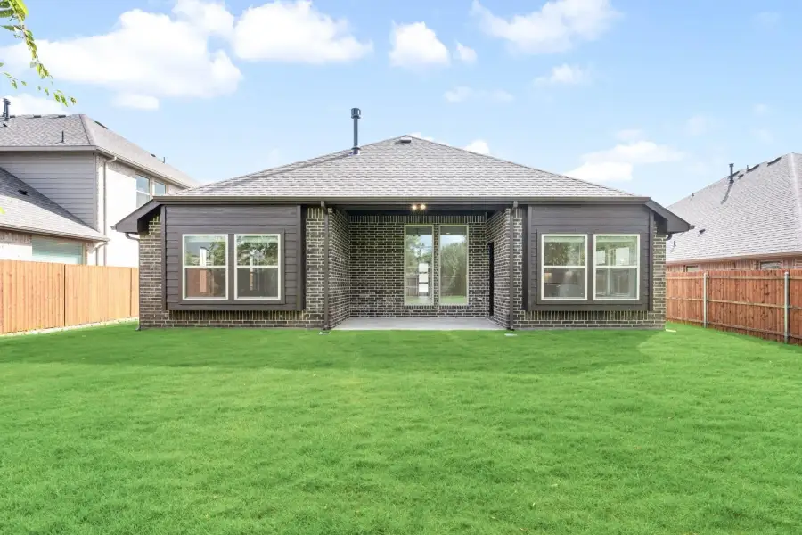 Rear exterior of single-story brick home with covered patio, large windows, and fenced backyard lawn.