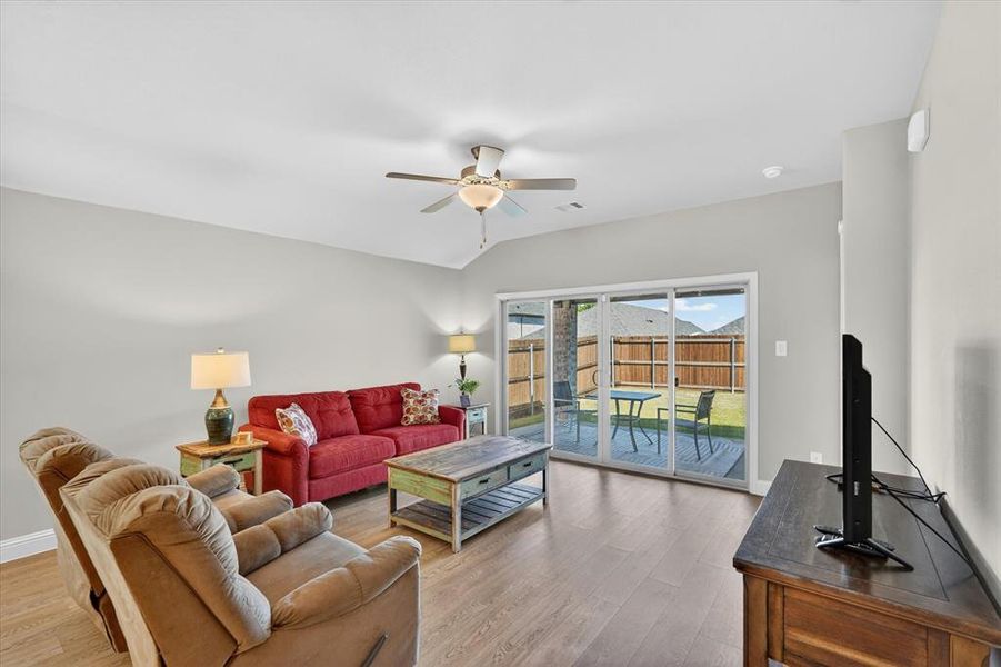 Open concept living area featuring wood-finish flooring, light gray walls, and a vaulted ceiling with a ceiling fan Open concept living area featuring wood-finish flooring, light gray walls, and a vaulted ceiling with a ceiling fan