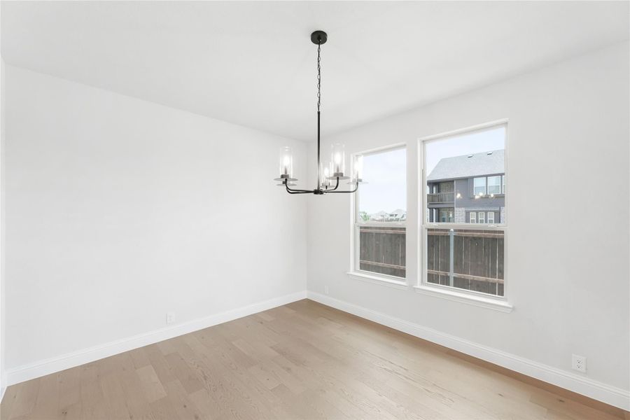 Empty dining room with light hardwood floors, black chandelier, and two windows with neighborhood view. Empty dining room with light hardwood floors, black chandelier, and two windows with neighborhood view.
