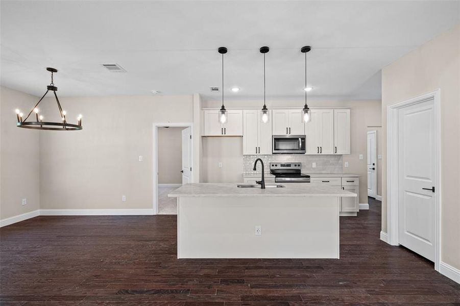 Open-concept living area featuring rich wood-finish flooring, a contemporary kitchen island with a light-toned countertop, white shaker-style cabinetry, and stainless steel appliances