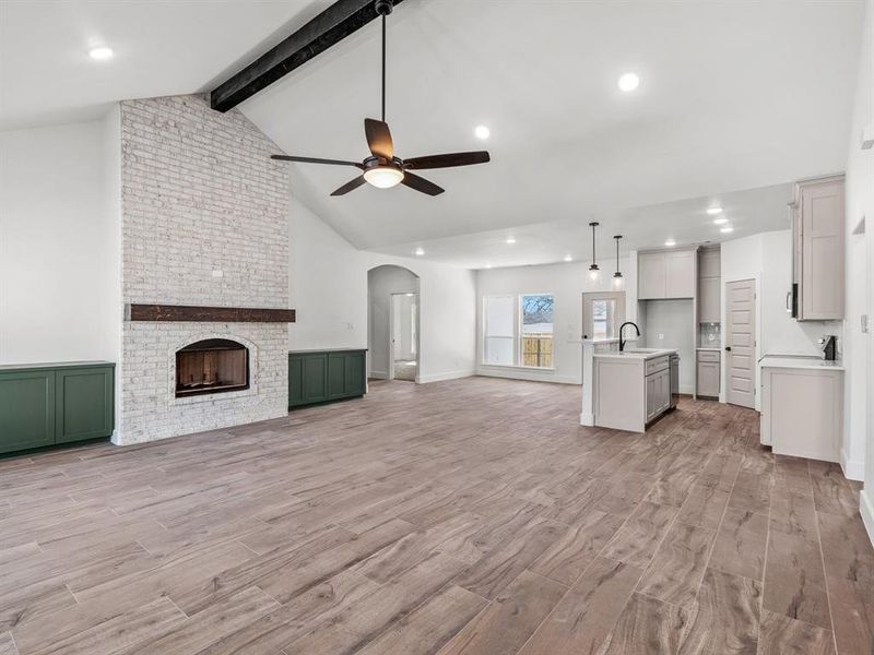 Unfurnished living room with beam ceiling, high vaulted ceiling, a sink, light wood finished floors, and ceiling fan