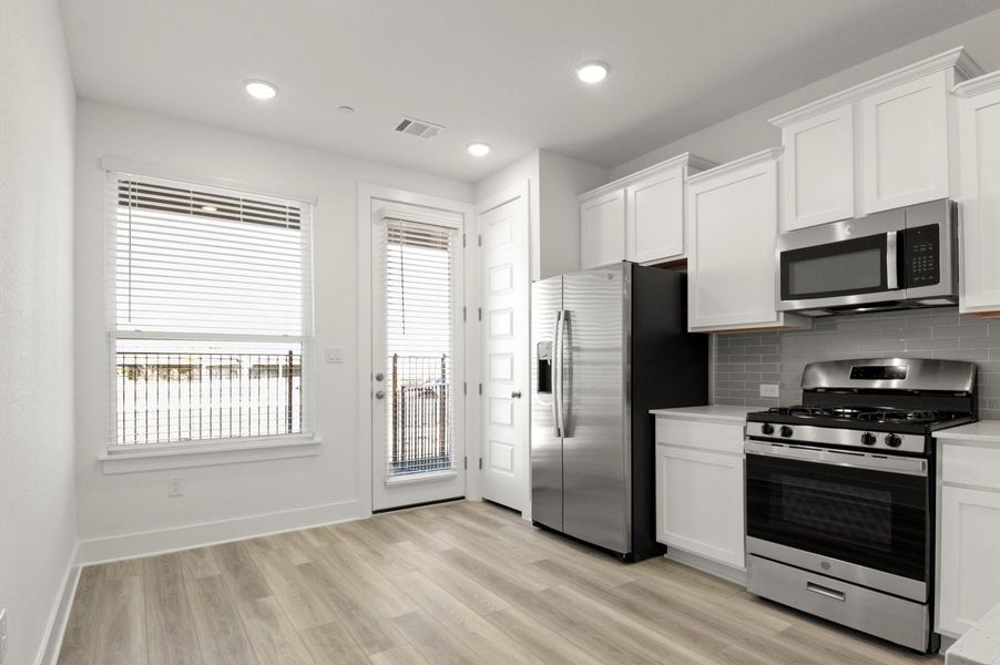 Kitchen featuring appliances with stainless steel finishes, white cabinetry, light wood finished floors, backsplash, and recessed lighting