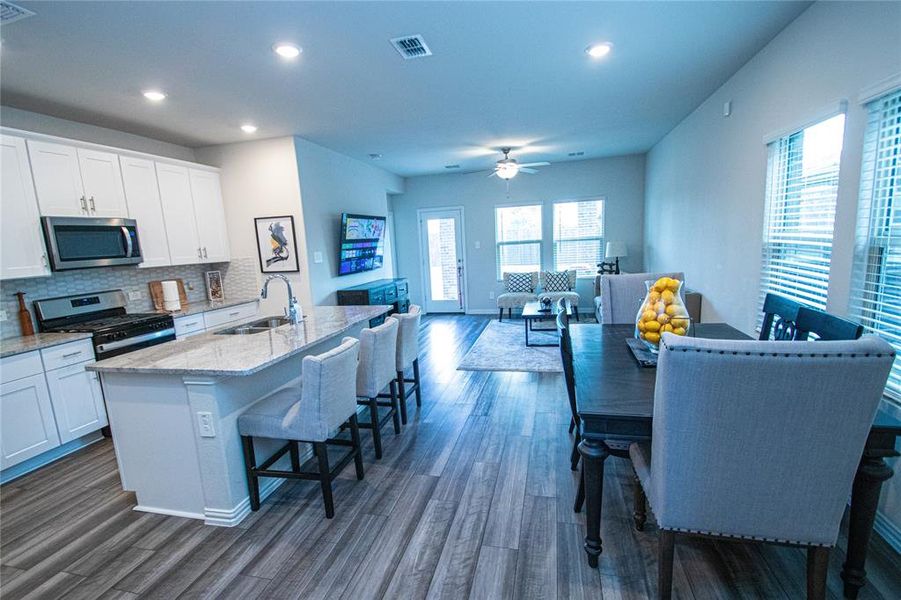 Kitchen with stainless steel appliances, white cabinetry, light stone counters, a kitchen island with sink, and tasteful backsplash Kitchen with stainless steel appliances, white cabinetry, light stone counters, a kitchen island with sink, and tasteful backsplash