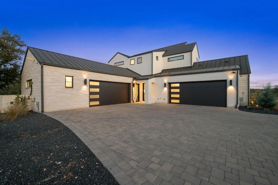 Contemporary home with a standing seam roof, an attached garage, stone siding, metal roof, and decorative driveway Contemporary home with a standing seam roof, an attached garage, stone siding, metal roof, and decorative driveway