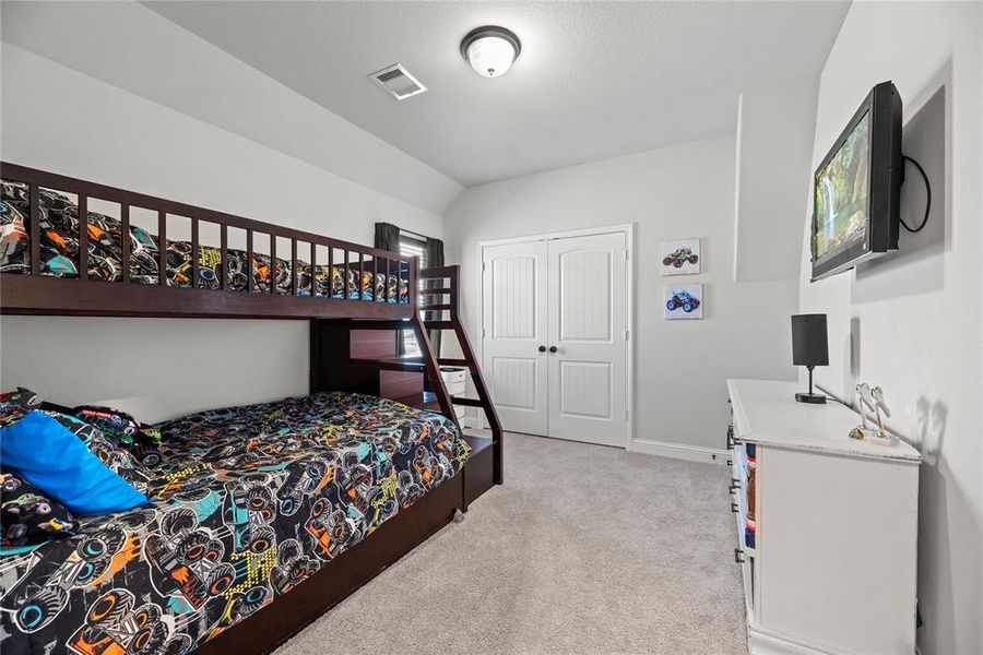 The room has neutral walls, carpeted flooring, and receives ample lighting from a ceiling fixture. It also includes a closet with white double doors, offering storage space.