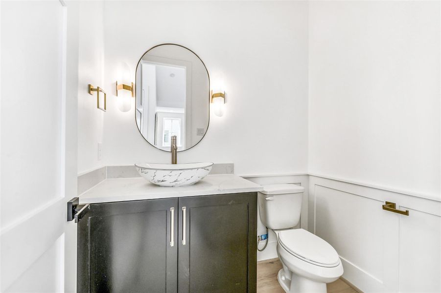 A statement of refined simplicity, this second-floor powder room features a custom floating vanity with shaker cabinetry, topped with a marble-inspired vessel sink and paired with a sleek brushed brass faucet. Elegant modern sconces flank the arched mirror, casting a soft ambient glow that complements the crisp white millwork wainscoting.Every design detail—from the hardware to the lighting—reflects thoughtful craftsmanship, seamlessly blending functionality with boutique hotel–level sophistication.