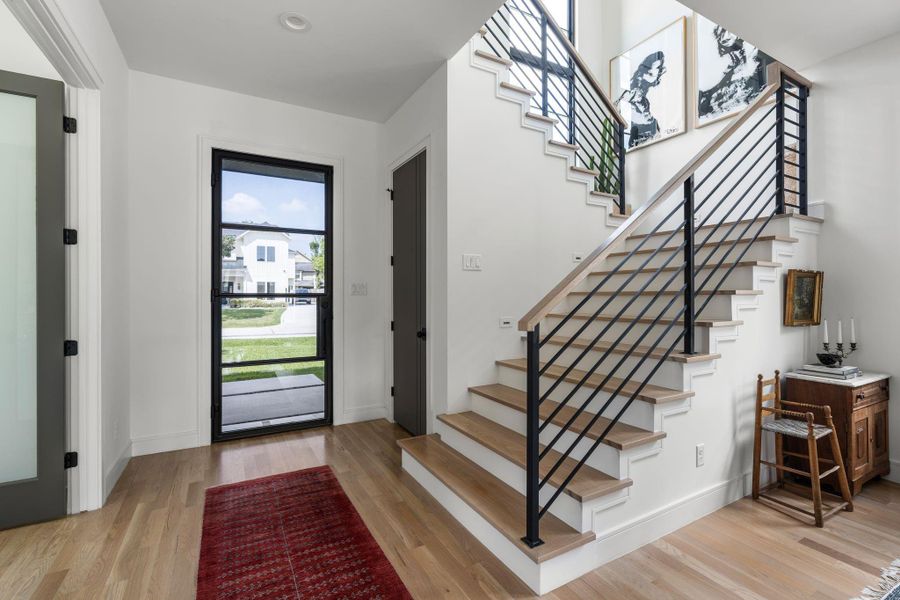 The entryway opens with hardwood floors, a modern staircase with iron railing, and a chandelier above, creating a bright first impression as you walk in. To the right is a huge walk in closet that continues under the stairs. To the left is double doors to a flex space for either a home office or downstairs bedroom with full bathroom next to it.