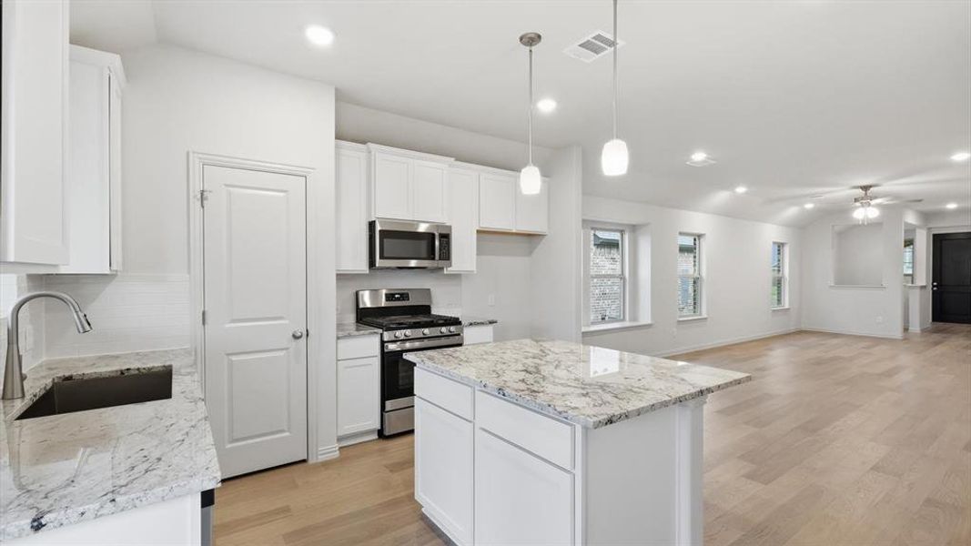 Open-concept kitchen and living area featuring white cabinetry, light-toned wood-finish flooring, a kitchen island with pendant lighting, stainless steel appliances, and recessed lighting throughout