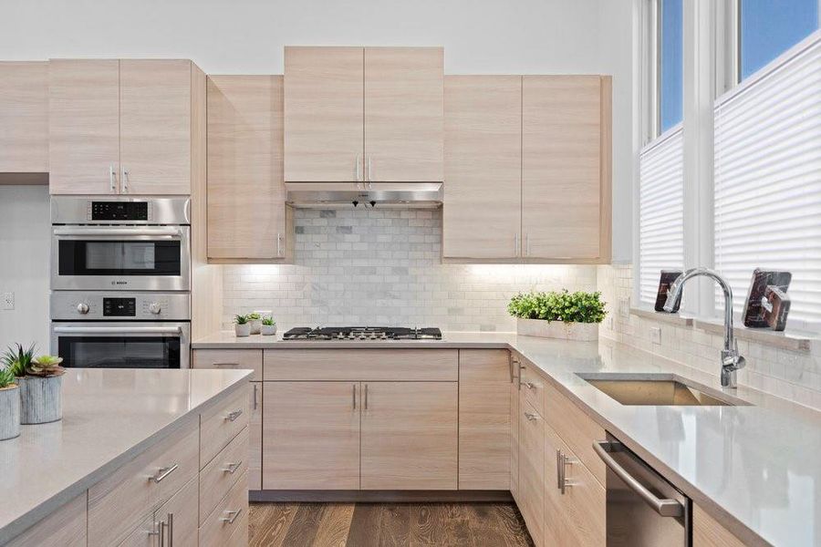 Kitchen featuring light brown cabinetry, light stone counters, stainless steel appliances, and tasteful backsplash