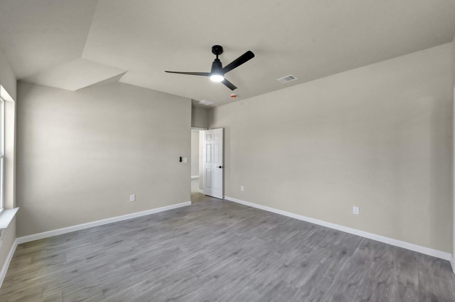 Primary bedroom suite offering a generous layout with clean lines, durable flooring, and a large window providing views of the backyard.