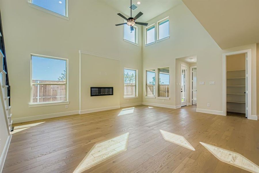 Unfurnished living room with light wood finished floors, a towering ceiling, a glass covered fireplace, and ceiling fan