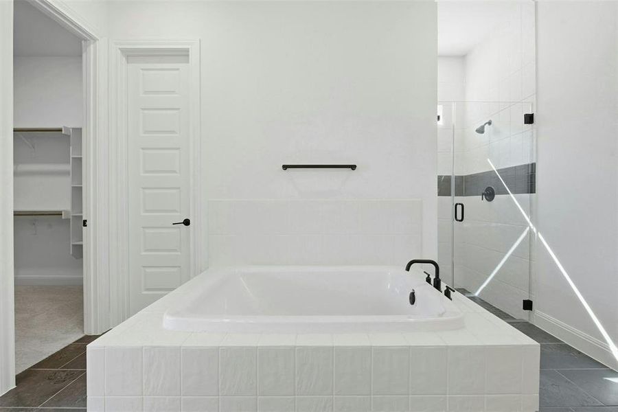 Expansive bathroom featuring a tiled soaking tub with black fixtures, a walk-in shower with clear glass enclosure and dark accent tile, and dark floor tile