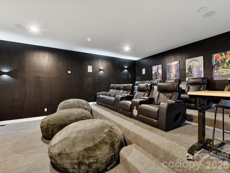 Private theater room featuring tiered stadium seating, sleek dark finishes, and a large projection screen for an immersive viewing experience.