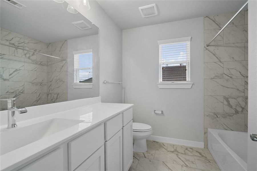 Secondary bath features tile flooring, bath/shower combo with tile surround, white stained wood cabinets, beautiful light countertops, mirror, dark, sleek fixtures and modern finishes.