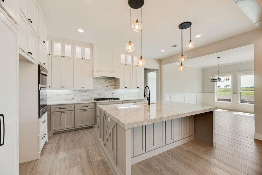 Kitchen featuring an island with sink, glass insert cabinets, light wood-style flooring, and hanging light fixtures