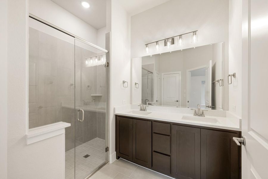 Bathroom with double sink vanity, dark wood cabinets, and glass-enclosed walk-in shower with tile walls