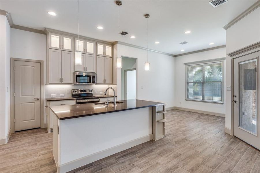 Kitchen featuring crown molding, glass insert cabinets, appliances with stainless steel finishes, hanging light fixtures, and tasteful backsplash Kitchen featuring crown molding, glass insert cabinets, appliances with stainless steel finishes, hanging light fixtures, and tasteful backsplash