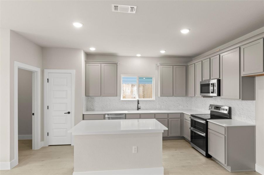 Kitchen with appliances with stainless steel finishes, gray cabinets, tasteful backsplash, light wood-style floors, and recessed lighting Kitchen with appliances with stainless steel finishes, gray cabinets, tasteful backsplash, light wood-style floors, and recessed lighting