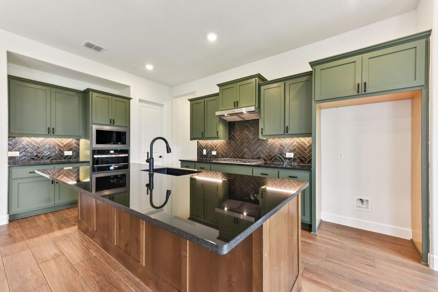 Kitchen featuring green cabinets, a kitchen island with sink, dark stone counters, light wood-style floors, and recessed lighting