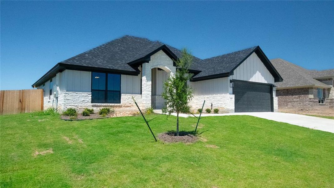 View of front of house with stone siding, driveway, a garage, and roof with shingles