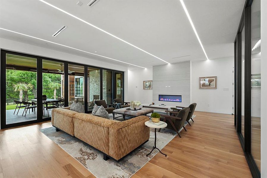 Spacious living area featuring wood-finish flooring, a linear electric fireplace with a textured surround, and recessed linear ceiling lighting