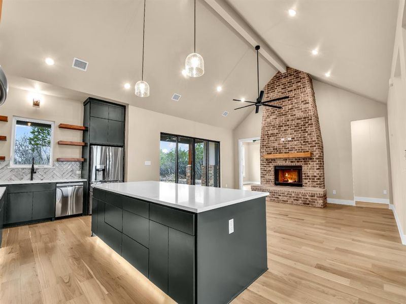 Kitchen with appliances with stainless steel finishes, backsplash, a fireplace, a center island, and hanging light fixtures