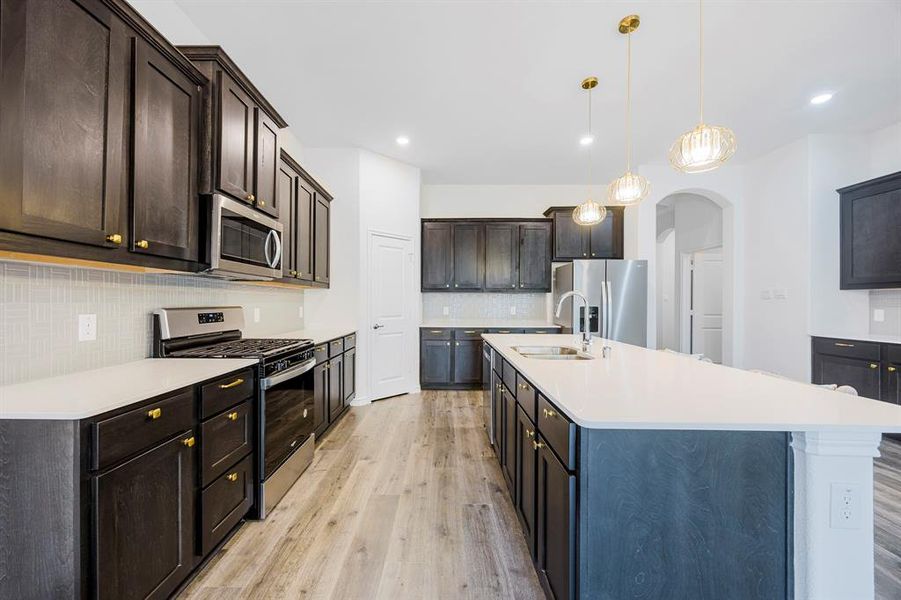 Kitchen with appliances with stainless steel finishes, sink, hanging light fixtures, dark brown cabinetry, and a kitchen island with sink