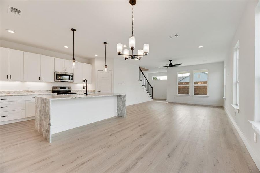 Kitchen with a chandelier, decorative light fixtures, light wood-style flooring, light stone countertops, and appliances with stainless steel finishes