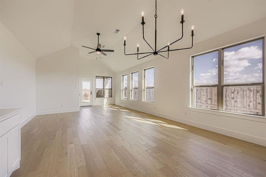 Unfurnished living room featuring a chandelier, high vaulted ceiling, light wood-style flooring, and a ceiling fan Unfurnished living room featuring a chandelier, high vaulted ceiling, light wood-style flooring, and a ceiling fan