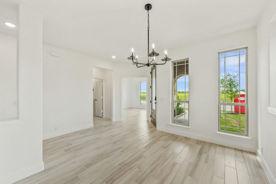 Empty dining room with black chandelier, light wood floors, and tall windows with yard view Empty dining room with black chandelier, light wood floors, and tall windows with yard view