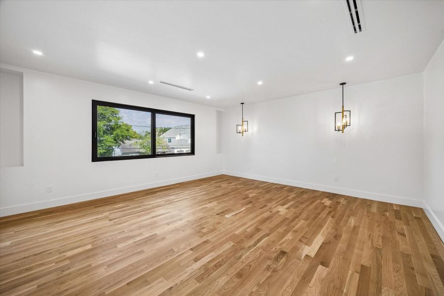 Primary bedroom featuring sleek hardwood floors, modern pendant lighting, and a large window offering natural light and scenic views. Primary bedroom featuring sleek hardwood floors, modern pendant lighting, and a large window offering natural light and scenic views.