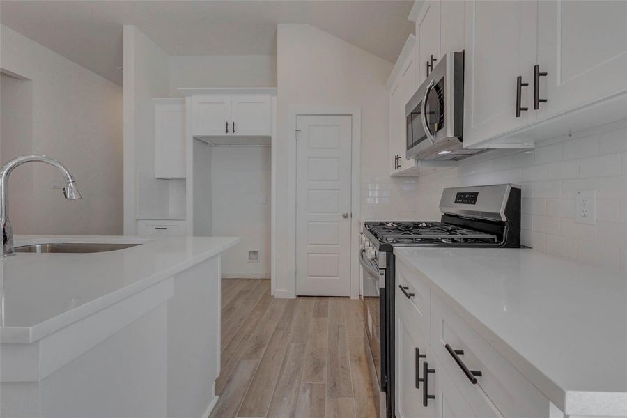 Highlighting efficiency and elegance, this view offers a glimpse of the walk-in pantry, additional cabinetry, and the home’s custom hardware. White subway tile backsplash adds texture behind the stainless steel gas range and microwave, while warm tile floors anchor the light, airy space.