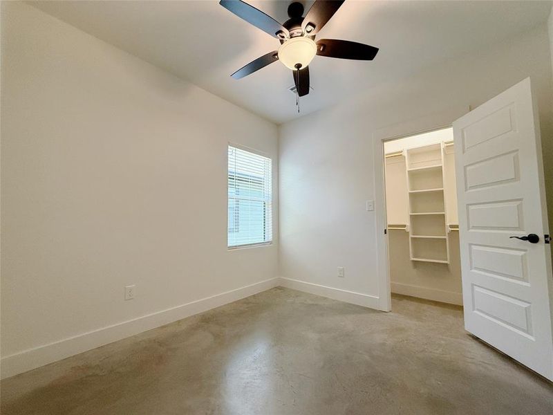 Unfurnished bedroom featuring finished concrete flooring, a spacious closet, and ceiling fan