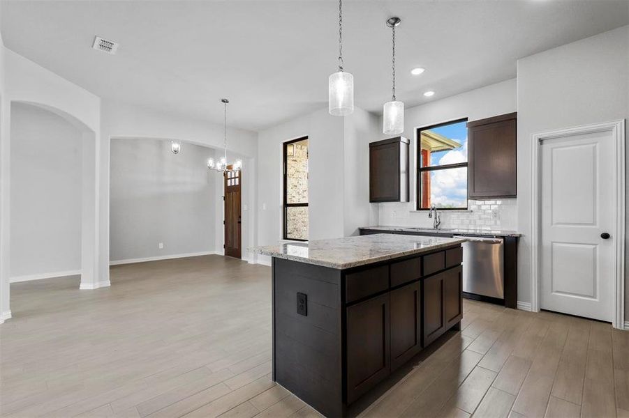 Kitchen featuring backsplash, a kitchen island, stainless steel dishwasher, light hardwood / wood-style floors, and hanging light fixtures