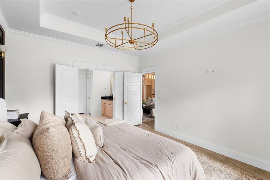 Bedroom with ensuite bathroom, crown molding, light hardwood / wood-style flooring, a notable chandelier, and a tray ceiling