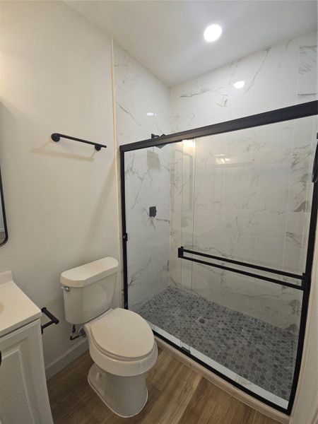 Bathroom with vanity, wood finished floors, baseboards, a marble finish shower, and toilet