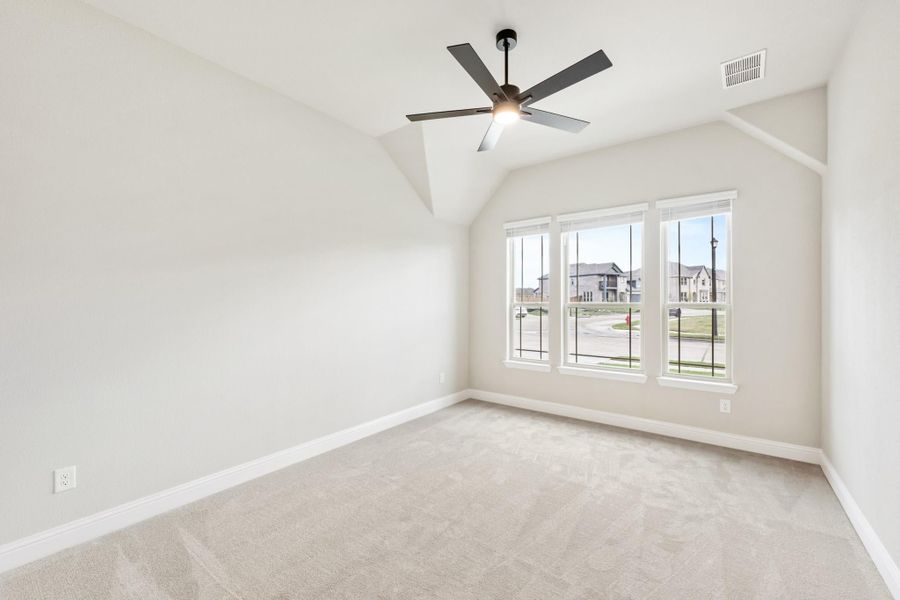 Empty bedroom with vaulted ceiling, ceiling fan, carpet flooring, and triple windows overlooking neighborhood