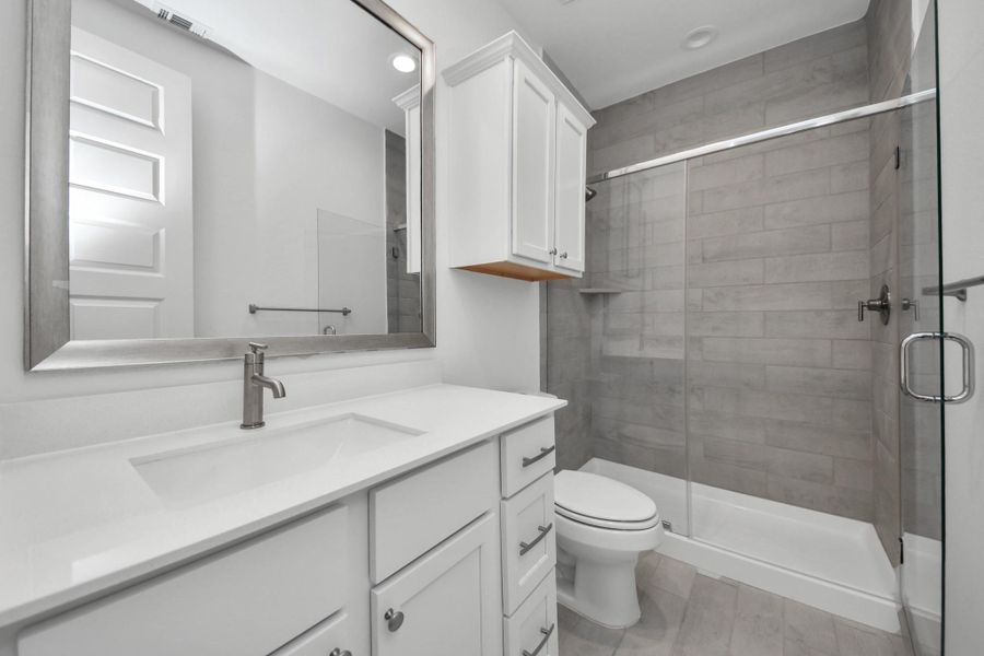 Secondary bath features tile flooring, walk-in shower with tile surround, light stained wood cabinets, beautiful light countertop.