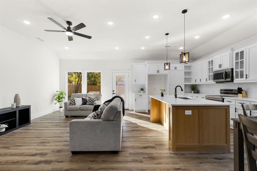 Kitchen featuring stainless steel appliances, decorative light fixtures, dark hardwood / wood-style floors, white cabinetry, and an island with sink