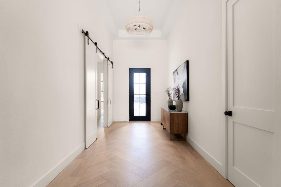 Herringbone hardwood floors lead to a sleek black glass-paneled entry door.