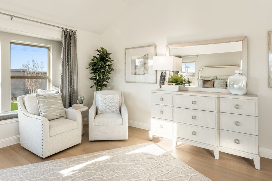 Bright bedroom sitting area with two white armchairs, white dresser with mirror, and hardwood floors