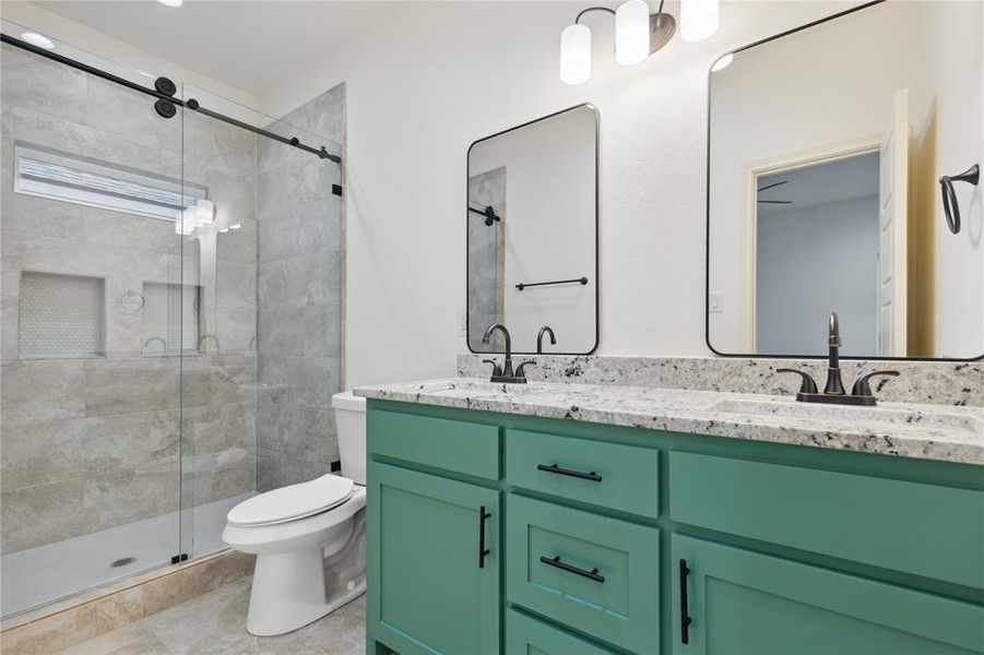 Bathroom featuring a shower with shower door, dual bowl vanity, tile flooring, and toilet