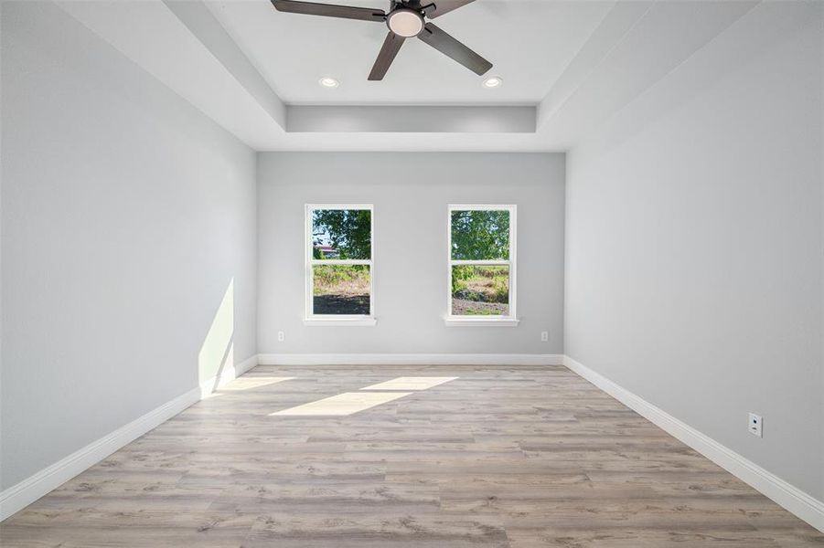 Empty room featuring a ceiling fan, wood finished floors, a raised ceiling, and recessed lighting Empty room featuring a ceiling fan, wood finished floors, a raised ceiling, and recessed lighting