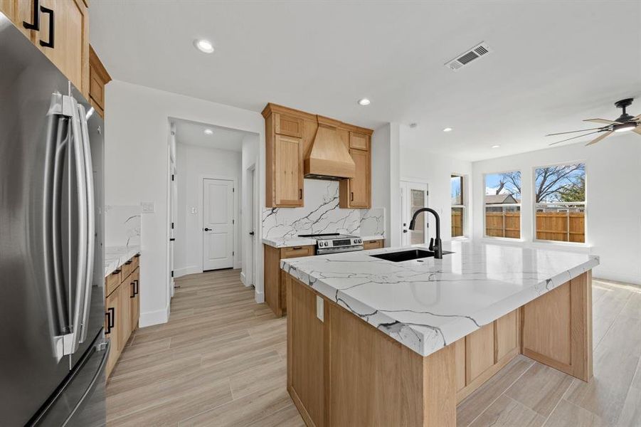 Kitchen with a kitchen island with sink, stainless steel appliances, premium range hood, a sink, and visible vents