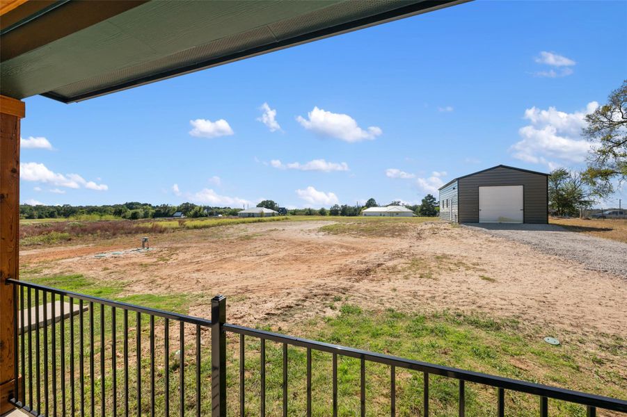 View of yard with a detached garage, an outbuilding, a balcony, and driveway